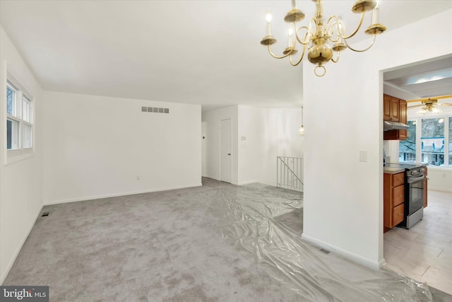 unfurnished living room with ceiling fan with notable chandelier, light colored carpet, and a wealth of natural light