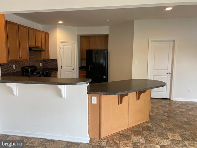 kitchen with a breakfast bar, black fridge, decorative backsplash, gas stove, and kitchen peninsula