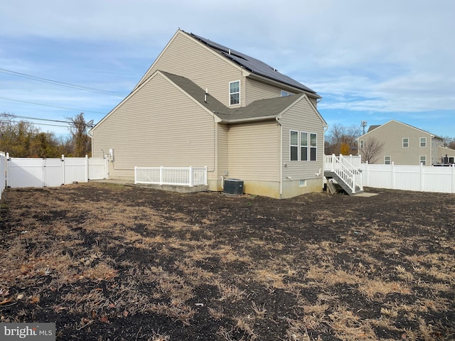 rear view of property with central AC unit and solar panels