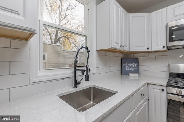 kitchen featuring decorative backsplash, appliances with stainless steel finishes, light stone counters, sink, and white cabinetry