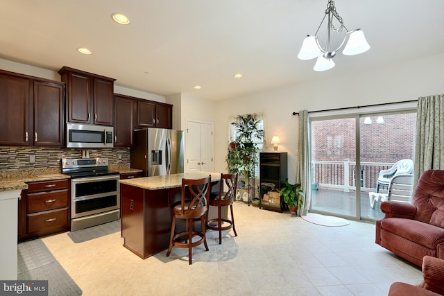 kitchen featuring light stone countertops, a center island, stainless steel appliances, decorative light fixtures, and a kitchen bar