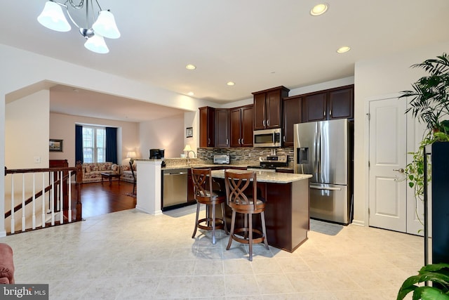 kitchen featuring hanging light fixtures, appliances with stainless steel finishes, dark brown cabinets, light stone counters, and kitchen peninsula