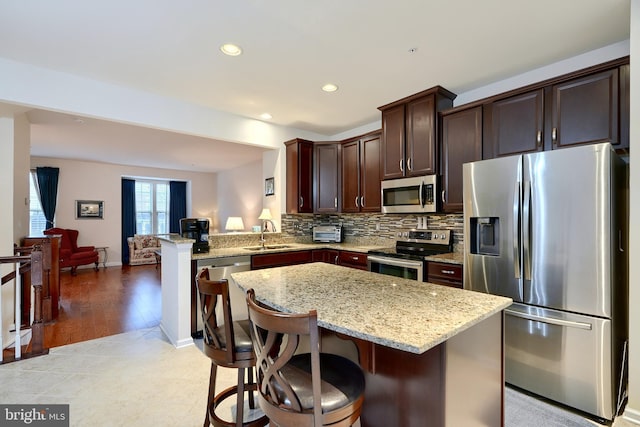 kitchen with a kitchen breakfast bar, sink, light wood-type flooring, a kitchen island, and stainless steel appliances