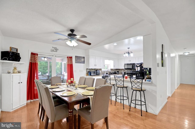 dining space with a textured ceiling, vaulted ceiling, light hardwood / wood-style floors, and ceiling fan with notable chandelier