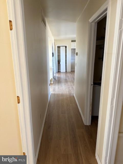 hall featuring visible vents, baseboards, and wood finished floors