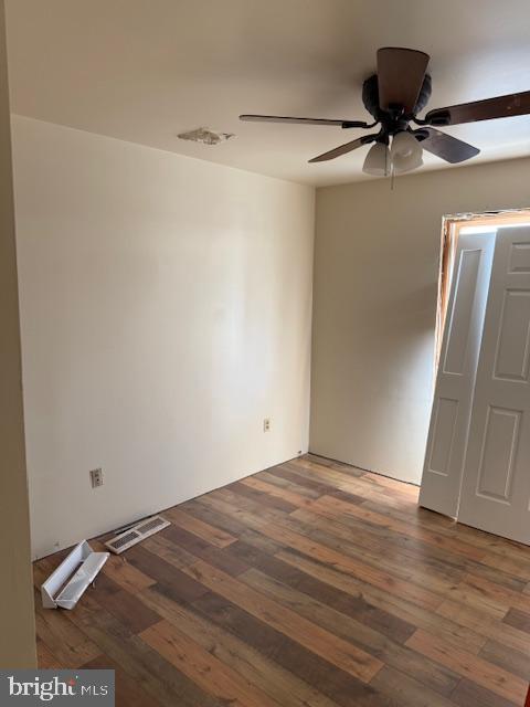 empty room featuring a ceiling fan, wood finished floors, and visible vents