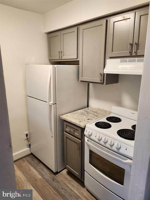 kitchen featuring gray cabinets, dark hardwood / wood-style flooring, white appliances, and light stone counters