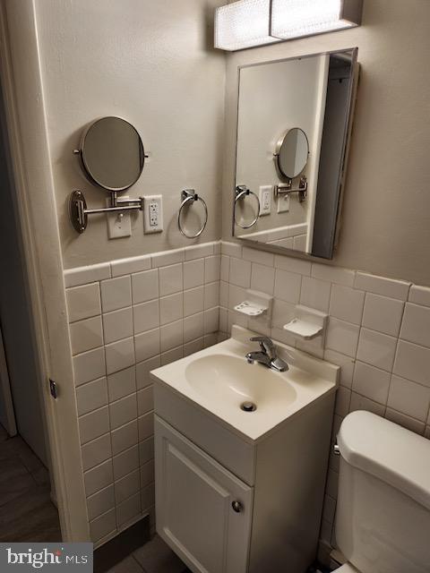 bathroom featuring vanity, toilet, and tile walls