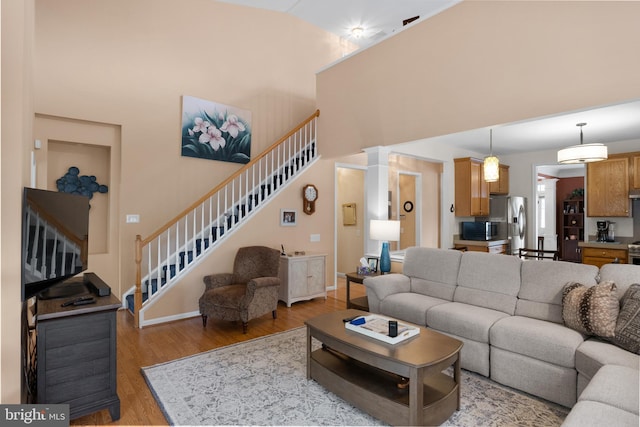 living room featuring decorative columns, high vaulted ceiling, and light wood-type flooring