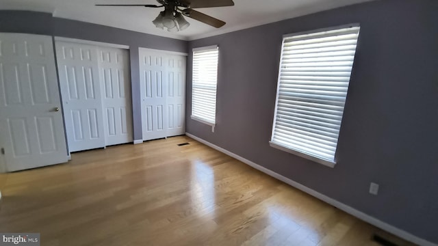 unfurnished bedroom featuring light hardwood / wood-style flooring, ceiling fan, multiple closets, and crown molding