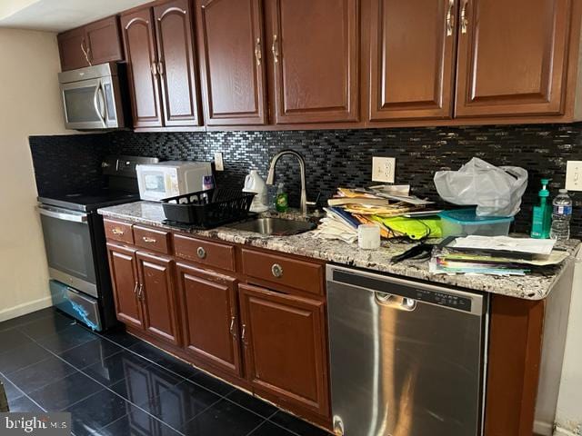 kitchen featuring dark tile patterned flooring, sink, appliances with stainless steel finishes, tasteful backsplash, and light stone counters