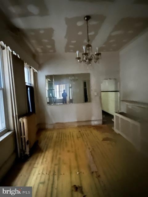 unfurnished living room featuring wood-type flooring, an inviting chandelier, and radiator