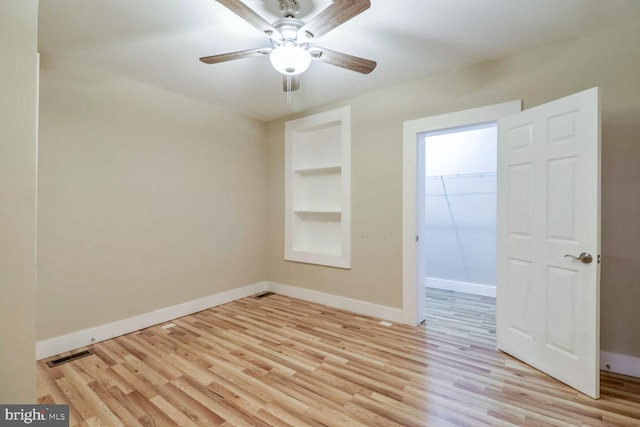 unfurnished room with built in features, light hardwood / wood-style flooring, and ceiling fan