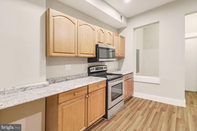 kitchen with light stone countertops, appliances with stainless steel finishes, electric panel, light brown cabinets, and light hardwood / wood-style floors