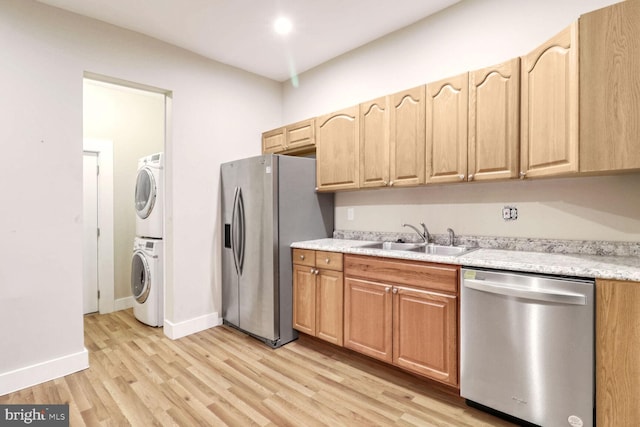 kitchen featuring light wood-type flooring, stacked washing maching and dryer, sink, and appliances with stainless steel finishes