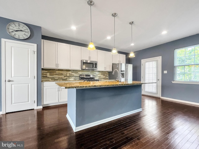 kitchen featuring stainless steel appliances, dark hardwood / wood-style floors, pendant lighting, a kitchen island with sink, and white cabinets