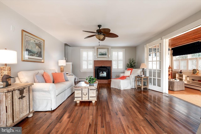 living room featuring dark hardwood / wood-style flooring, a brick fireplace, a baseboard radiator, and ceiling fan