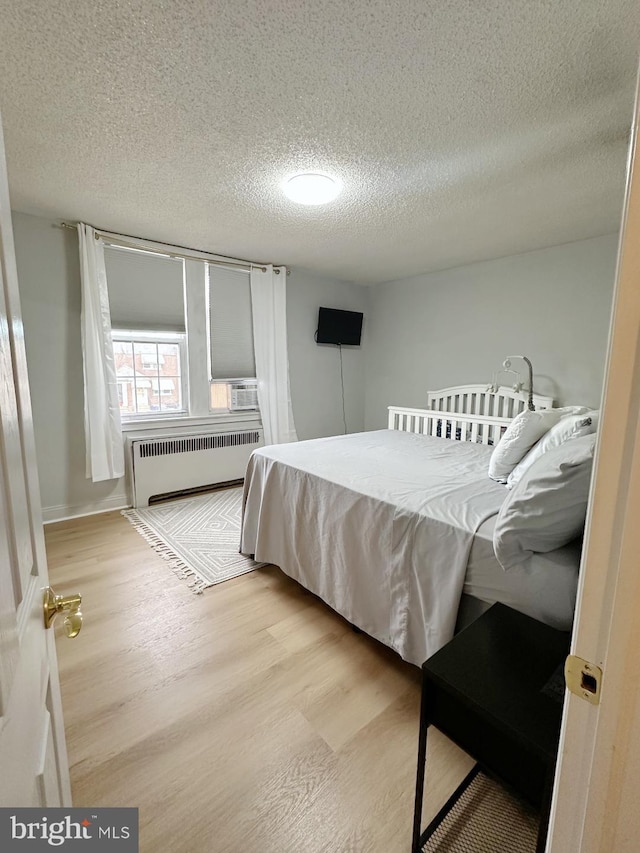 bedroom with radiator heating unit, a textured ceiling, and light hardwood / wood-style flooring