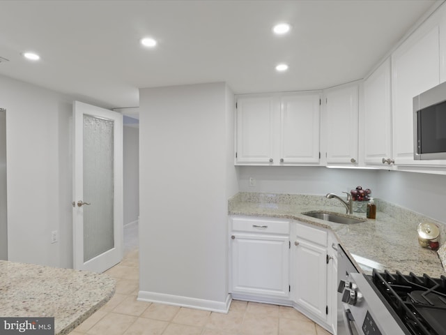 kitchen featuring white cabinetry, sink, light stone countertops, gas range oven, and light tile patterned floors