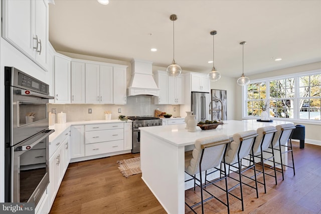 kitchen with premium appliances, premium range hood, dark hardwood / wood-style floors, and a center island with sink