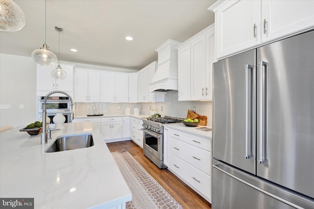 kitchen with custom exhaust hood, high end appliances, white cabinets, hanging light fixtures, and hardwood / wood-style flooring