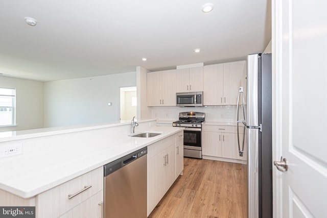 kitchen with sink, backsplash, kitchen peninsula, light hardwood / wood-style floors, and appliances with stainless steel finishes