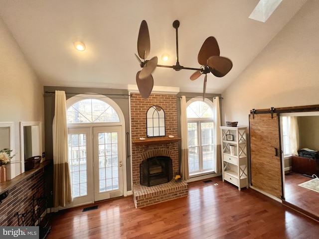 unfurnished living room featuring hardwood / wood-style floors, visible vents, a skylight, a barn door, and a brick fireplace