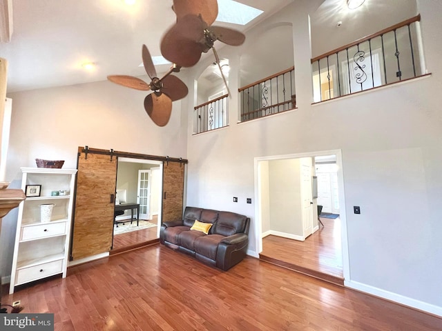 living area featuring a skylight, a barn door, wood finished floors, and a ceiling fan