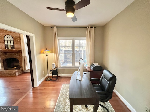 office featuring a ceiling fan, wood finished floors, a fireplace, and baseboards