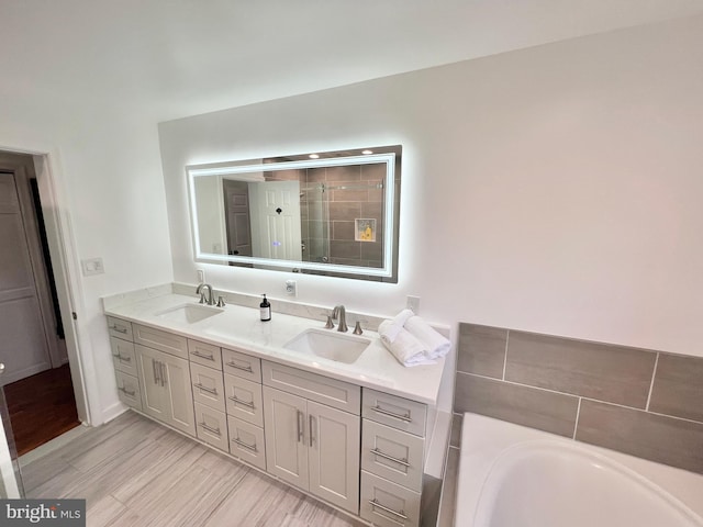 full bathroom featuring double vanity, a stall shower, a bathtub, and a sink