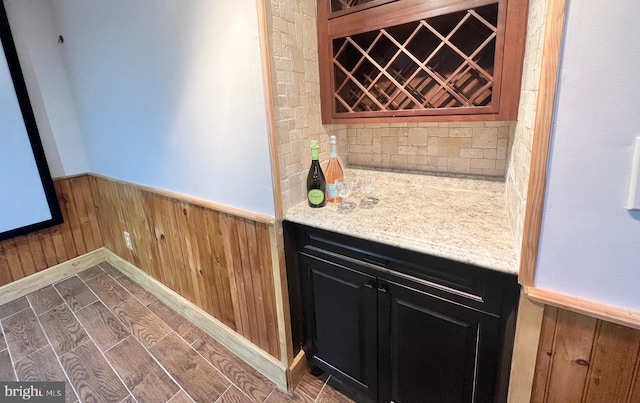 wine room featuring wood finish floors, a wainscoted wall, a bar, and wood walls