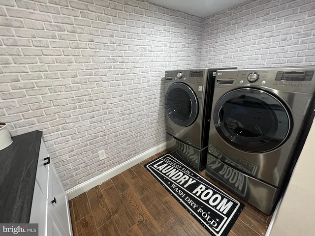 laundry room with washing machine and clothes dryer, brick wall, baseboards, laundry area, and wood finished floors