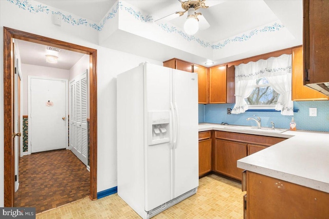 kitchen featuring ceiling fan, sink, a raised ceiling, white refrigerator with ice dispenser, and backsplash