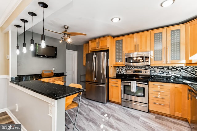 kitchen with ceiling fan, stainless steel appliances, kitchen peninsula, dark stone countertops, and a breakfast bar