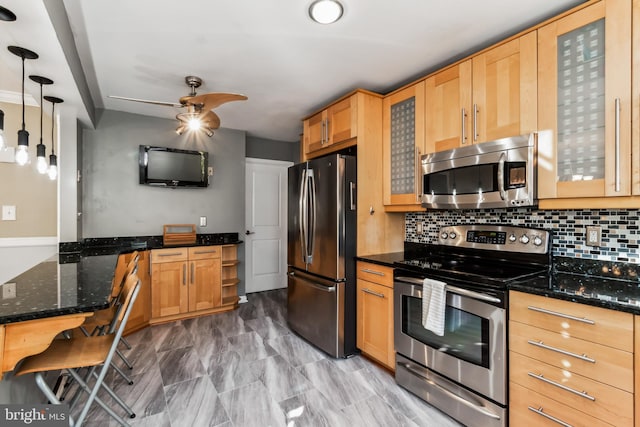 kitchen featuring backsplash, hanging light fixtures, ceiling fan, dark stone countertops, and stainless steel appliances