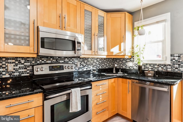 kitchen featuring sink, decorative backsplash, dark stone countertops, appliances with stainless steel finishes, and decorative light fixtures