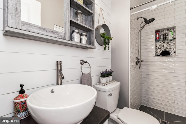 bathroom with tiled shower, toilet, and sink