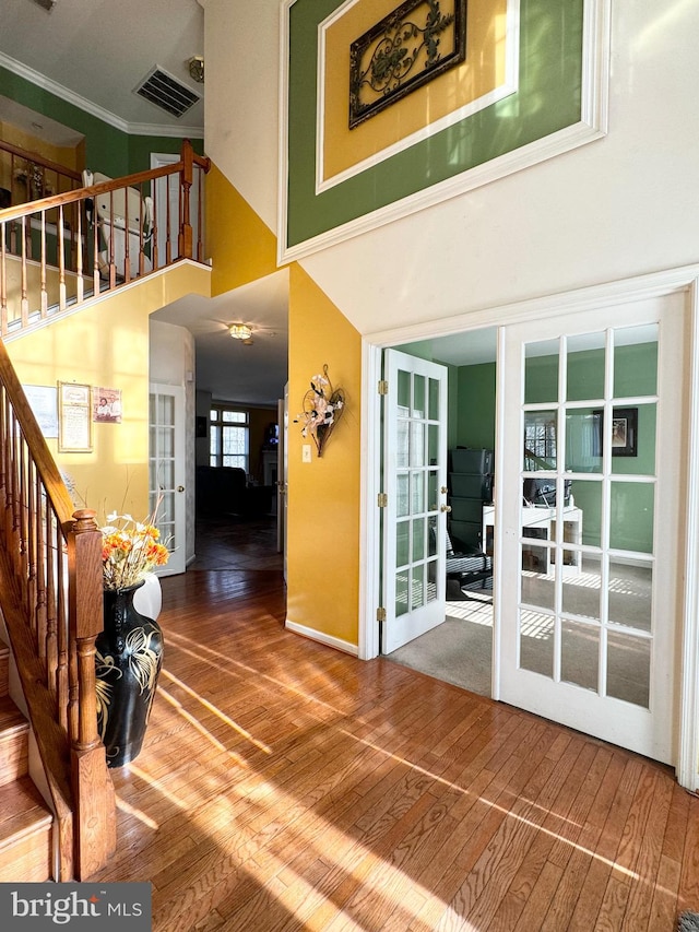 interior space with french doors, a towering ceiling, wood-type flooring, and ornamental molding