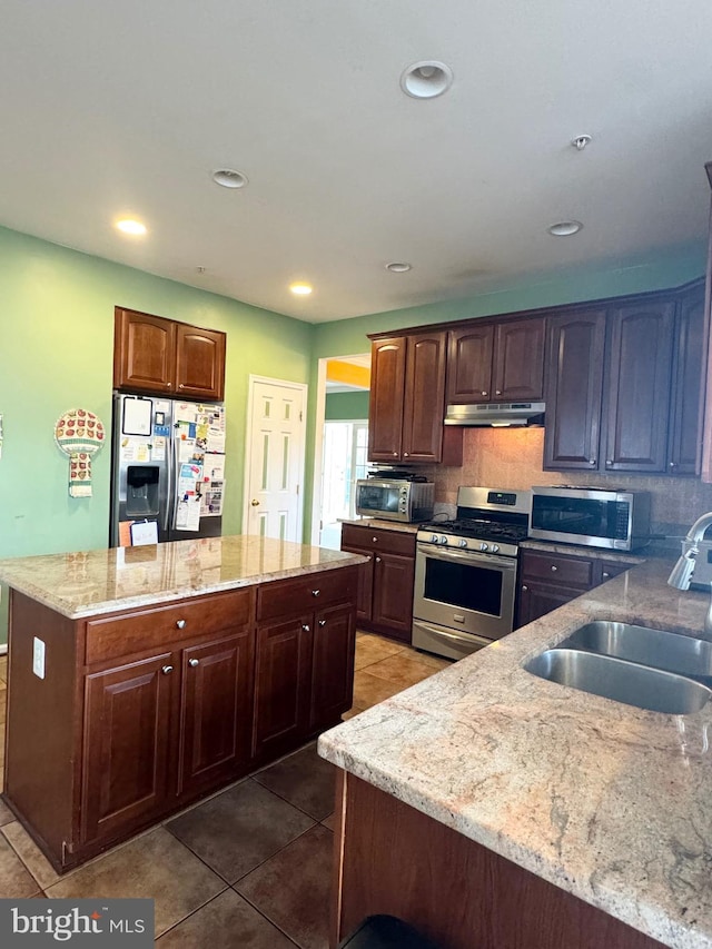 kitchen featuring decorative backsplash, appliances with stainless steel finishes, light stone counters, sink, and dark tile patterned flooring