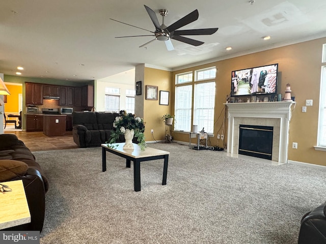 carpeted living room featuring a tile fireplace, crown molding, and ceiling fan