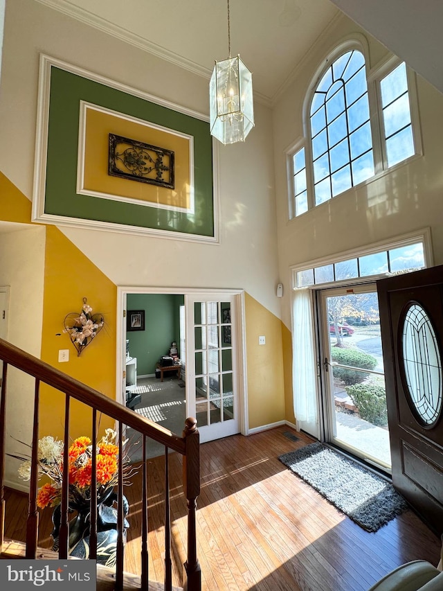 entryway with wood-type flooring, crown molding, a towering ceiling, and a chandelier