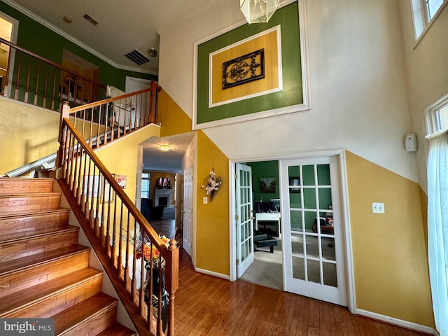 stairs featuring wood-type flooring, french doors, ornamental molding, and a high ceiling