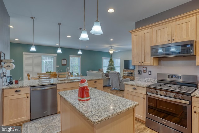 kitchen featuring stainless steel appliances, ceiling fan, sink, pendant lighting, and a kitchen island