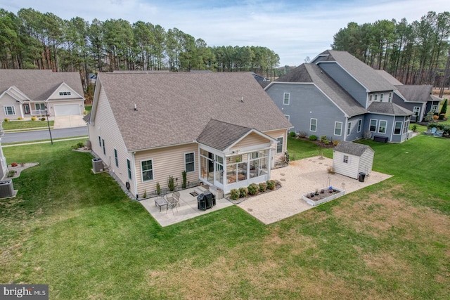 rear view of house with a sunroom, a lawn, a shed, central AC unit, and a patio