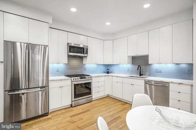 kitchen with appliances with stainless steel finishes, white cabinetry, light hardwood / wood-style flooring, and sink