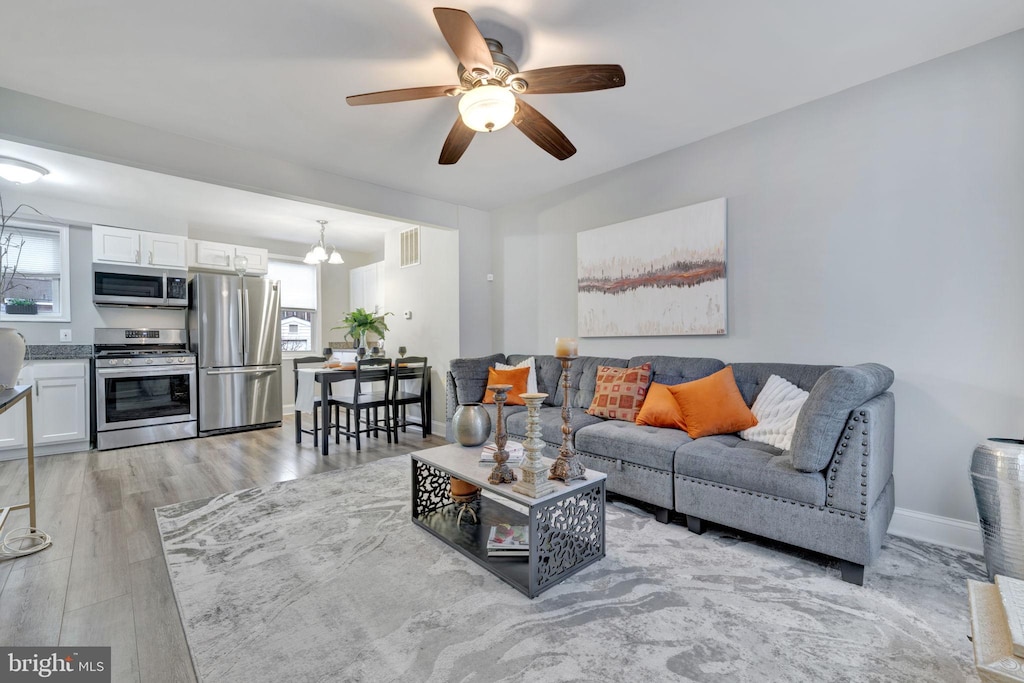 living room with a healthy amount of sunlight, ceiling fan with notable chandelier, and light wood-type flooring