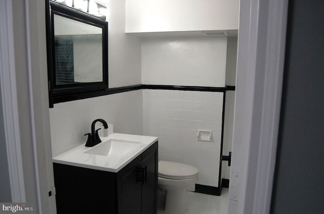 bathroom featuring vanity, toilet, and tile walls