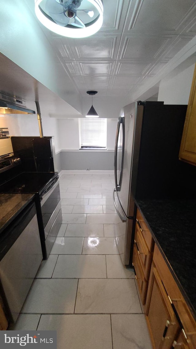 kitchen featuring exhaust hood, dark stone counters, decorative light fixtures, light tile patterned flooring, and stainless steel appliances