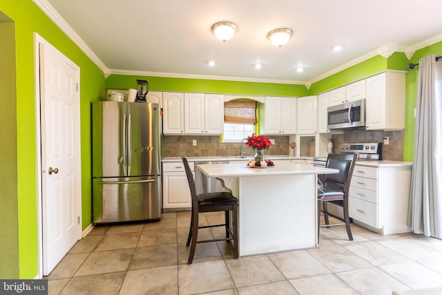 kitchen featuring white cabinetry, a center island, a kitchen bar, appliances with stainless steel finishes, and ornamental molding