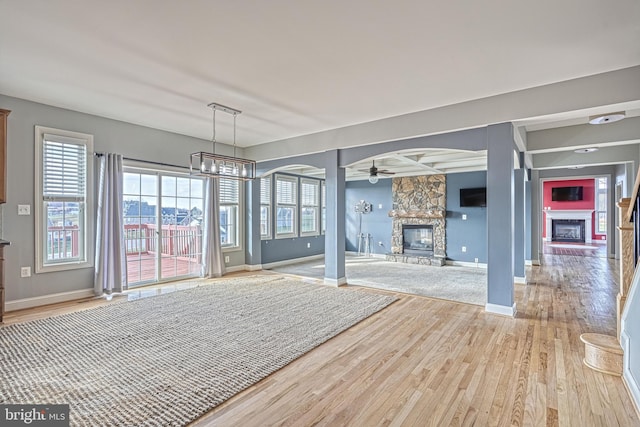 interior space with a stone fireplace, beamed ceiling, light hardwood / wood-style floors, and ceiling fan with notable chandelier